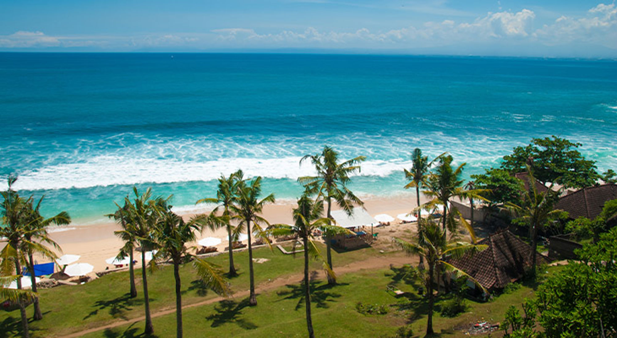 Balangan Beach Bali Uitzicht op tropisch strand met palmbomen, ligbedden en blauwe zee.