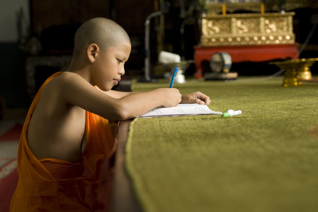 Jonge monnik schrijft in een schrift in een Thaise tempel tijdens een groepsrondreis door Noord en Zuid Thailand.
