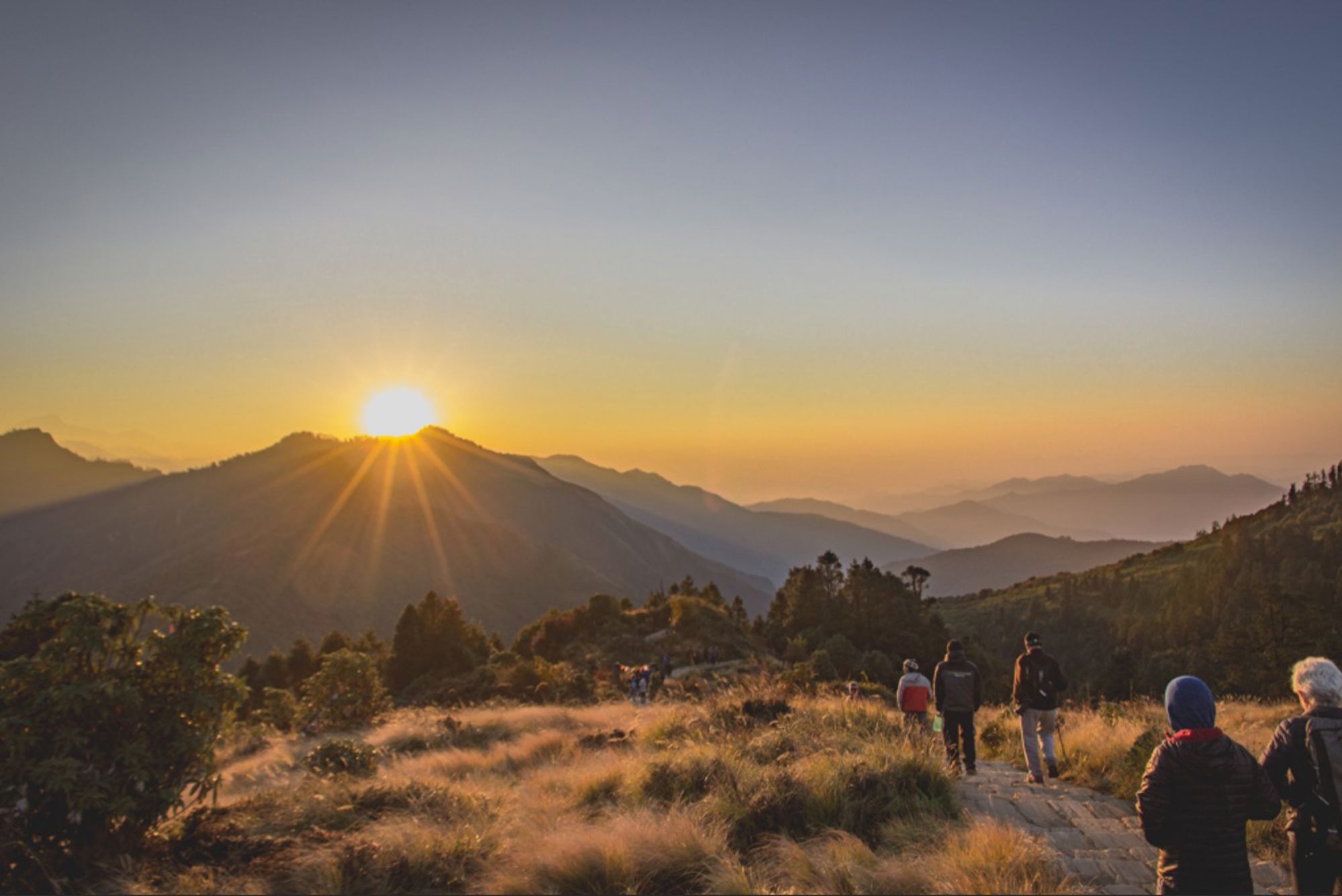 Zonsopgang boven de bergen in Nepal, met wandelaars op een pad door hoog gras.