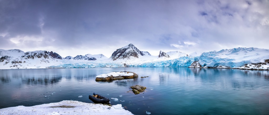 Gletsjerlandschap bij Spitsbergen met ijsblauwe gletsjer, besneeuwde bergen en zodiacboot op kalm water.