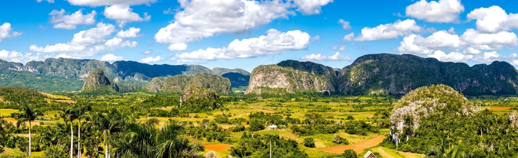 Groene vallei met mogotes en palmbomen in Viñales, Cuba, onder een blauwe lucht met wolken.