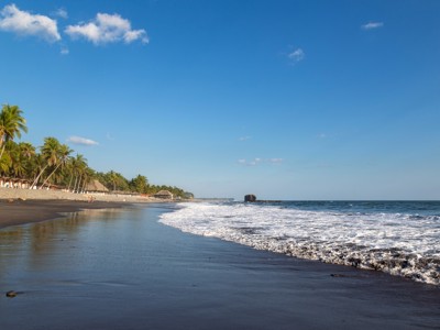 Zwart zandstrand met palmbomen en branding aan de Pacifische kust van El Salvador.