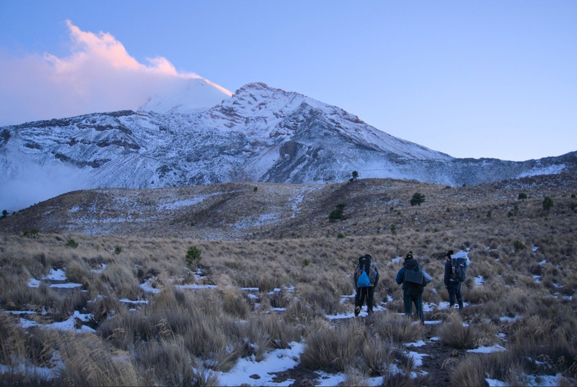 Wandelaars in een hoogvlakte met sneeuw richting de besneeuwde vulkaan Pico de Orizaba in Mexico.