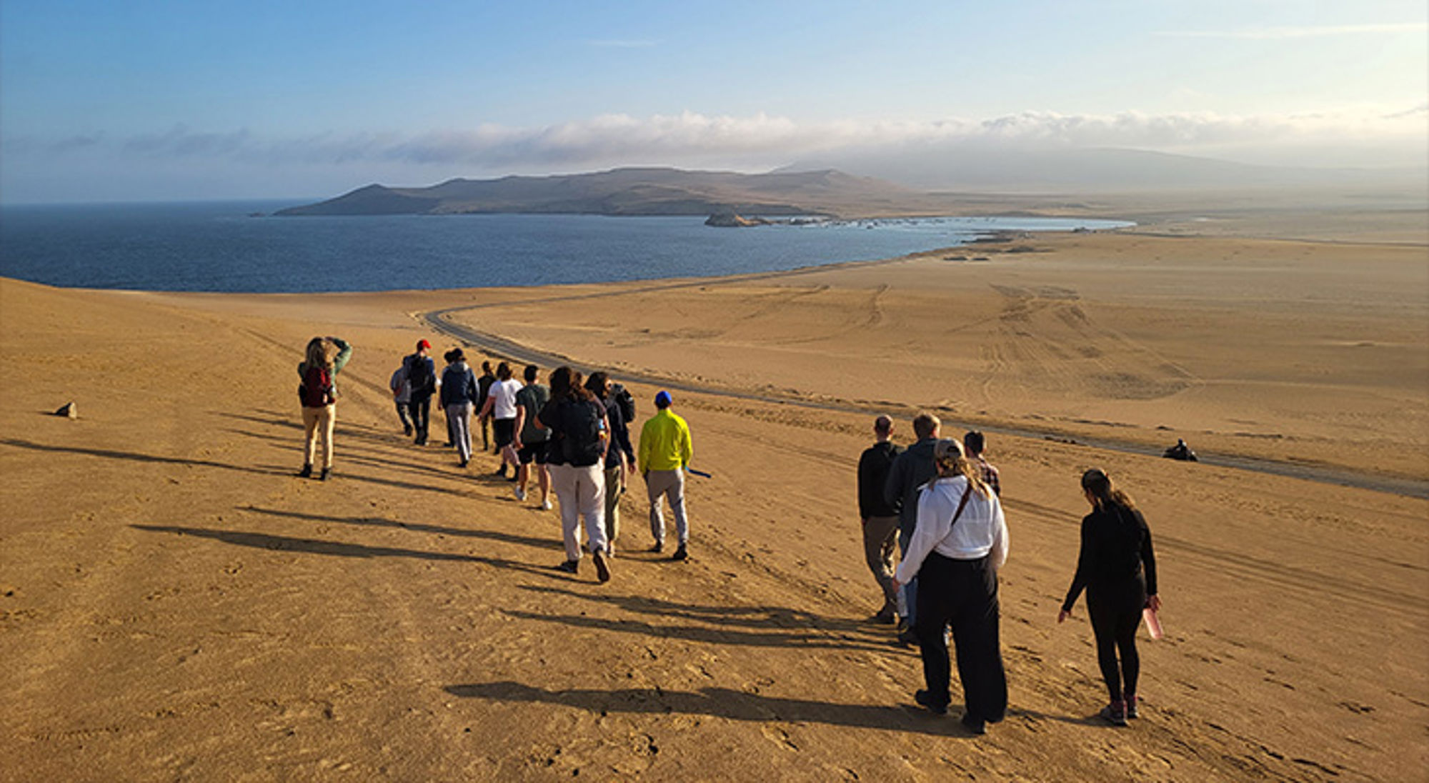 Paracas Groep wandelaars op zandduinen met uitzicht op zee en bergen.