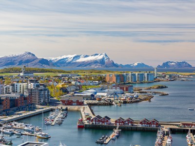 Uitzicht over de haven van Bodø met boten en kleurrijke huizen, met besneeuwde bergen op de achtergrond in Noorwegen.
