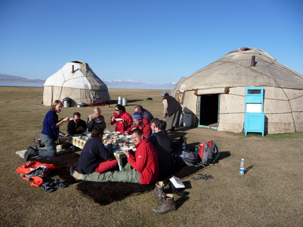 Groepsrondreis Kirgistan: reizigers lunchen bij een yurtkamp in de steppe, met bergen op de achtergrond.