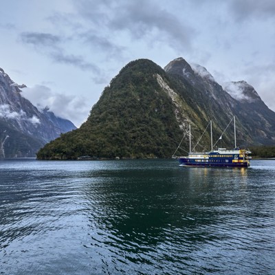 Cruiseschip in Milford Sound met hoge bergen en laaghangende wolken op de achtergrond.