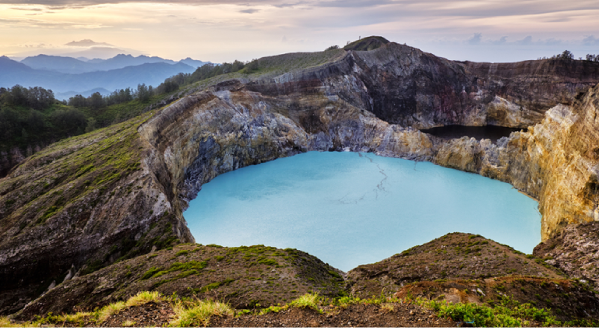 Mount Kelimutu op Flores Turquoise kratermeer in vulkanische caldera met rotswanden en bergen op de achtergrond.