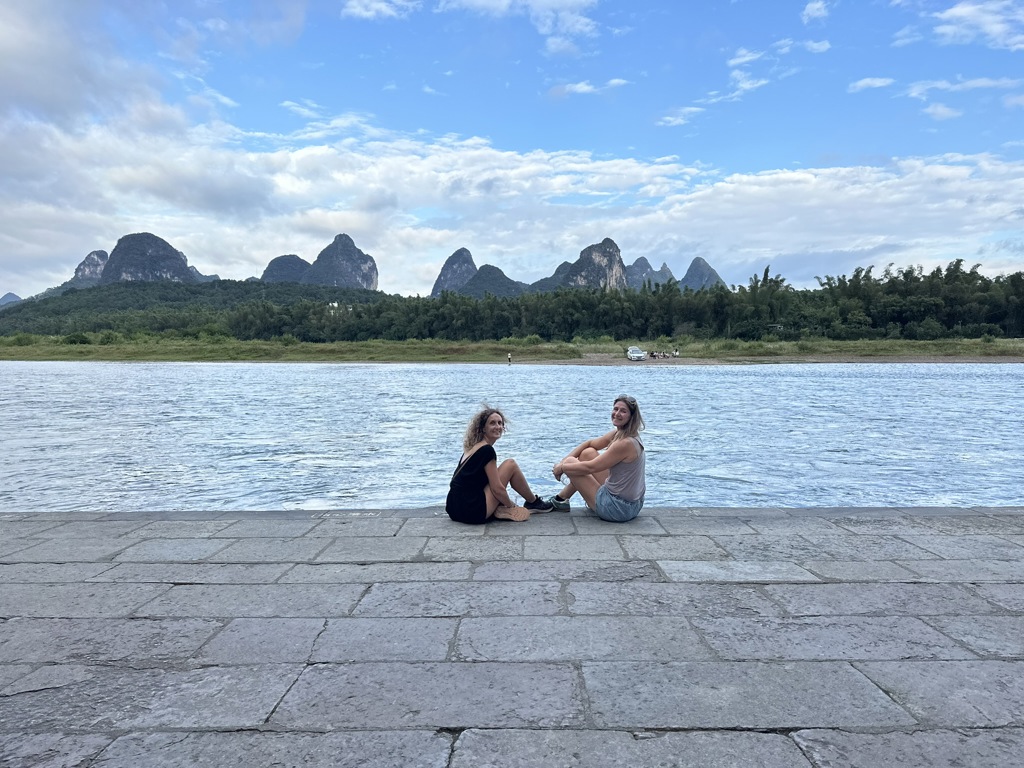 Twee reizigers aan de rivier met karstbergen op de achtergrond tijdens een familiereis in China.