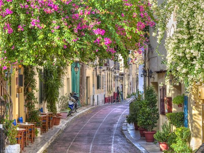 Sfeervol straatje in Griekenland met kleurrijke bougainvillea, terrasstoelen en traditionele gevels.