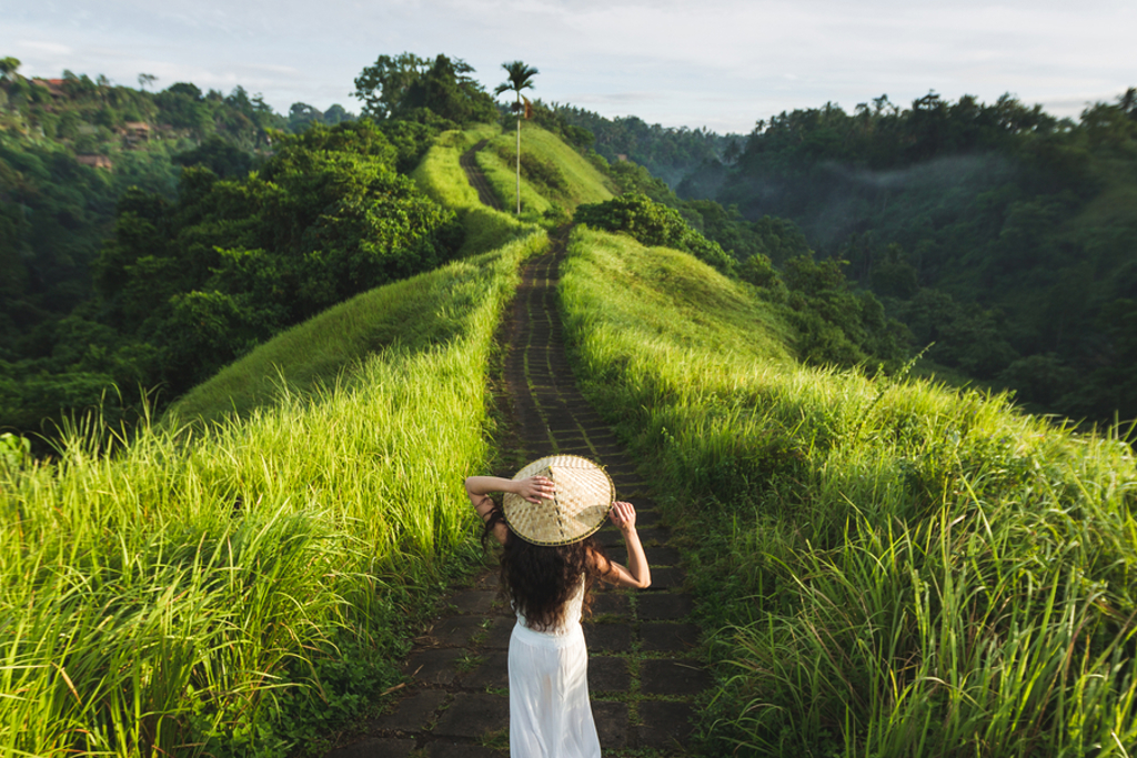 Vrouw met hoed wandelt over groen pad door rijstvelden op Bali, Indonesië.