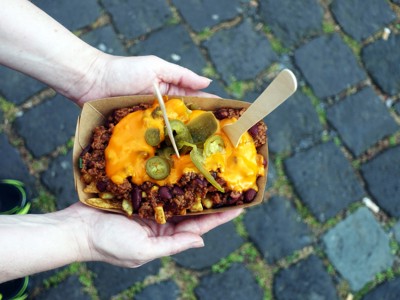 Poutine met kaas en jalapeño in een kartonnen bakje, vastgehouden boven kasseien in Oost-Canada.
