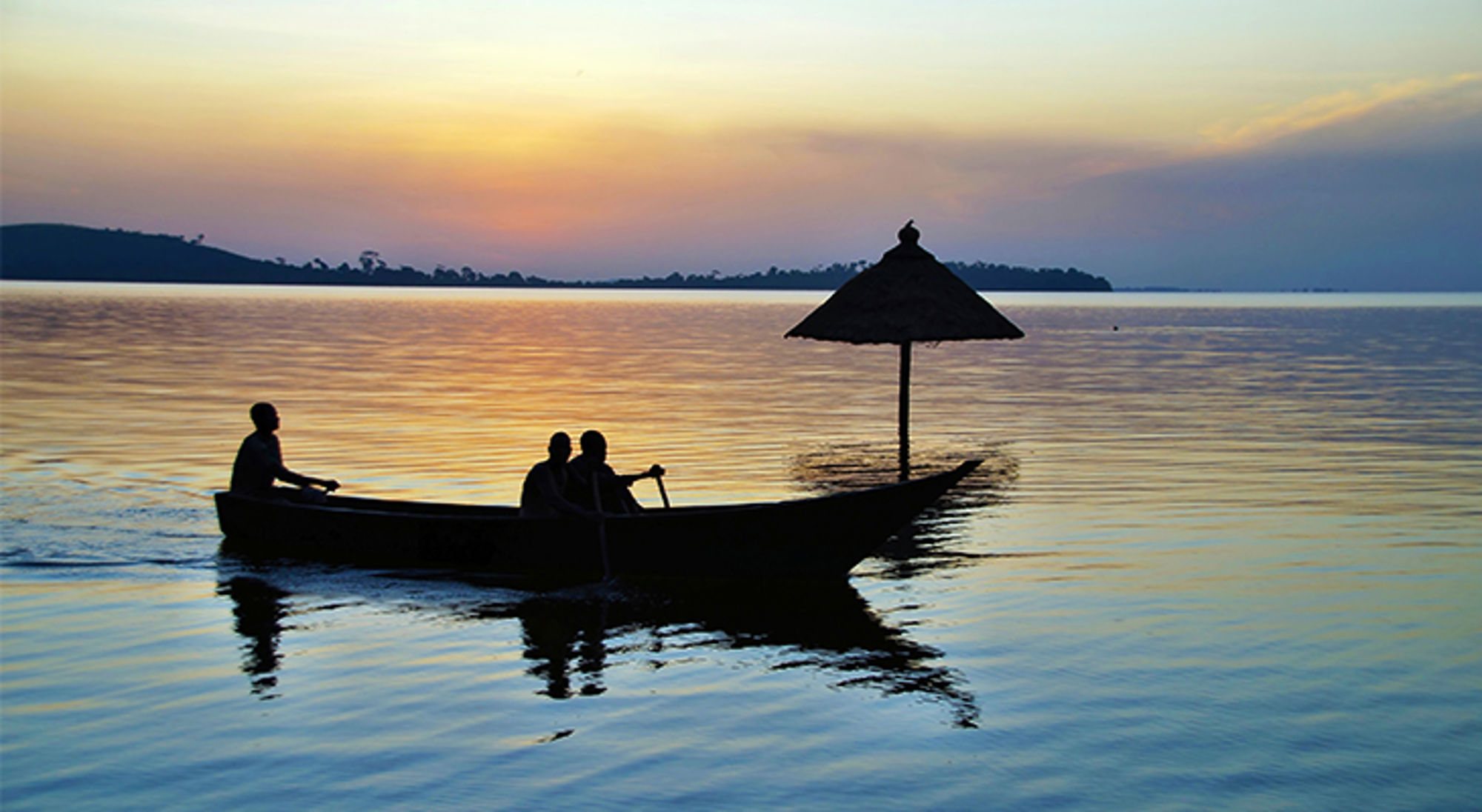 Boot met drie mensen op het Victoriameer bij zonsondergang, onderdeel van de Route Oeganda.
