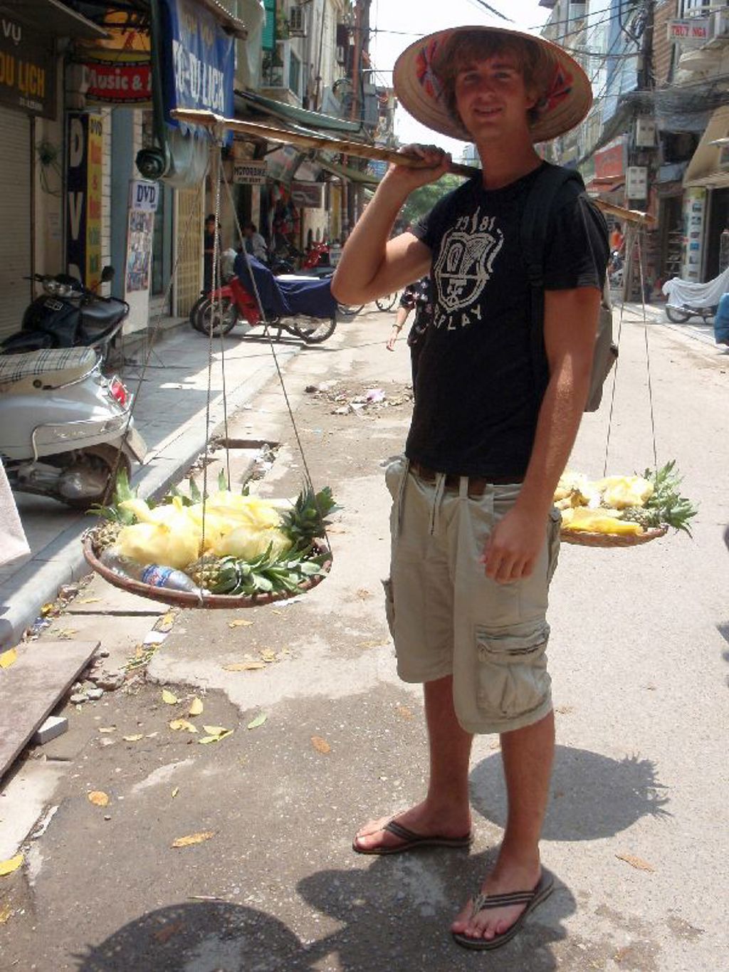 Reiziger met Vietnamese hoed draagt fruit aan een bamboestok in een straat in Vietnam.