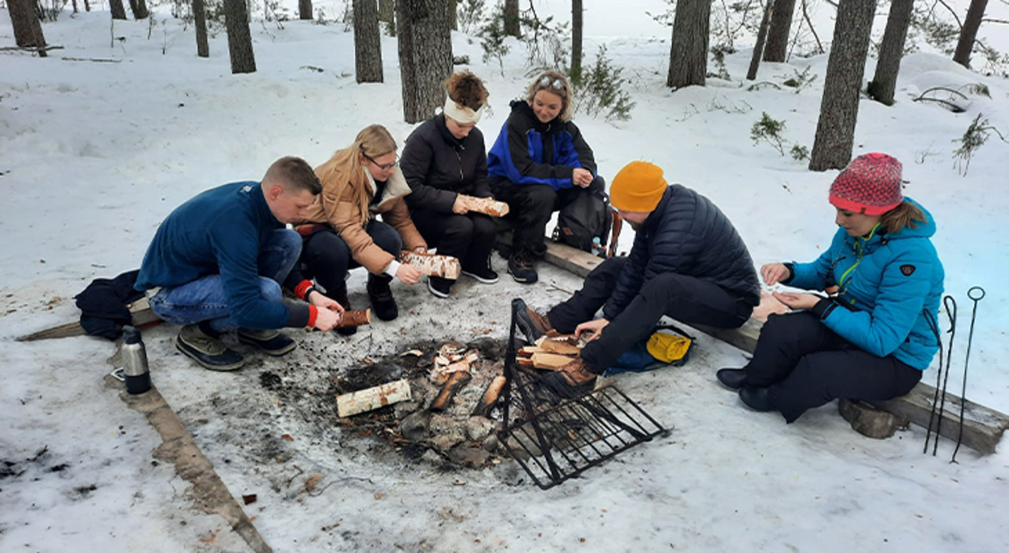 Kampvuur Finland Groep vrienden maakt eten bij een kampvuur in een besneeuwd bos.