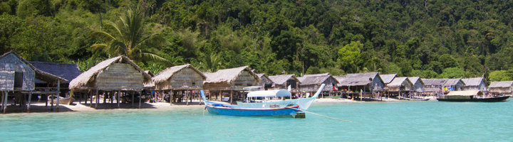 Houten paalwoningen en longtailboot aan een wit zandstrand in Mu Ko Chang National Park, Thailand.