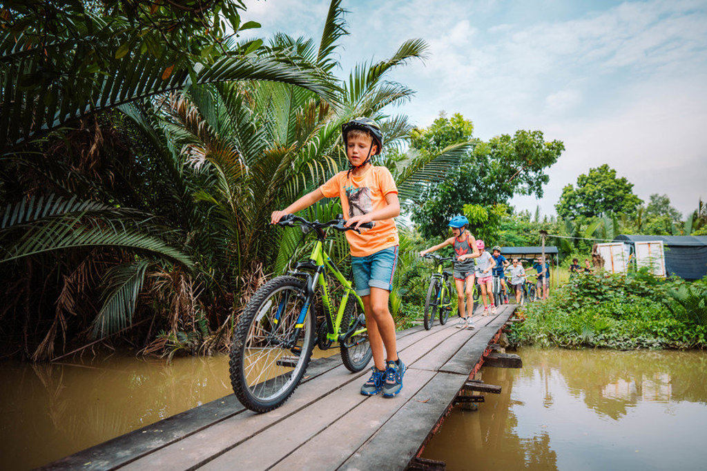 Kinderen fietsen over een houten brug door tropisch groen tijdens een familiereis in Thailand.