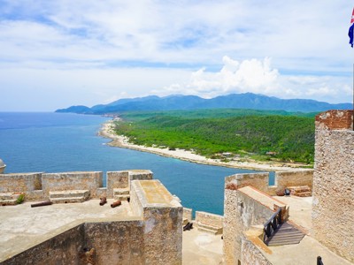 Uitzicht vanaf fort El Morro op de kustlijn en bergen bij Santiago de Cuba, met Cubaanse vlag.