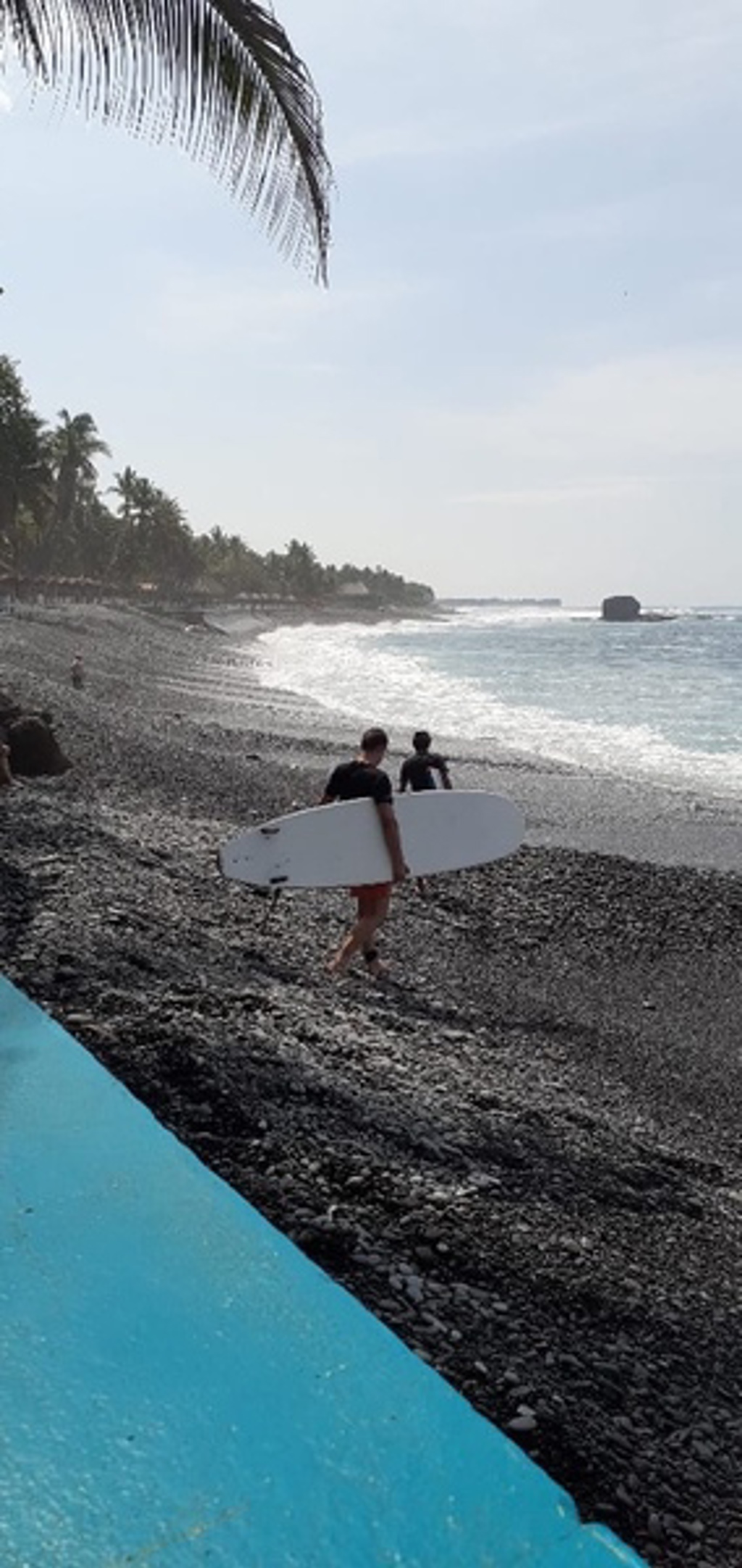 Surfers lopen met surfboards over een zwart zandstrand tijdens 22-35ers reis Guatemala, Honduras en El Salvador.