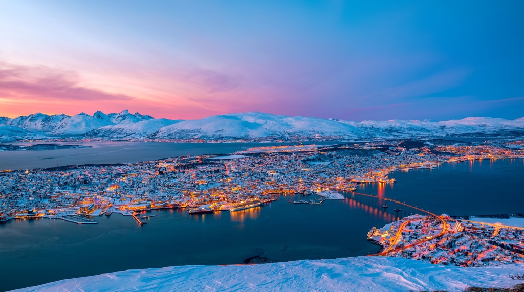 Uitzicht op Tromsø in Noorwegen met besneeuwde bergen en fjord bij zonsondergang.