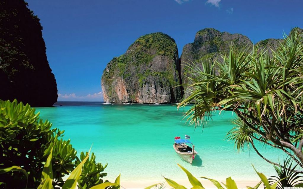 Tropisch strand in Thailand met turquoise zee, longtailboot en hoge kalksteenrotsen op de achtergrond.