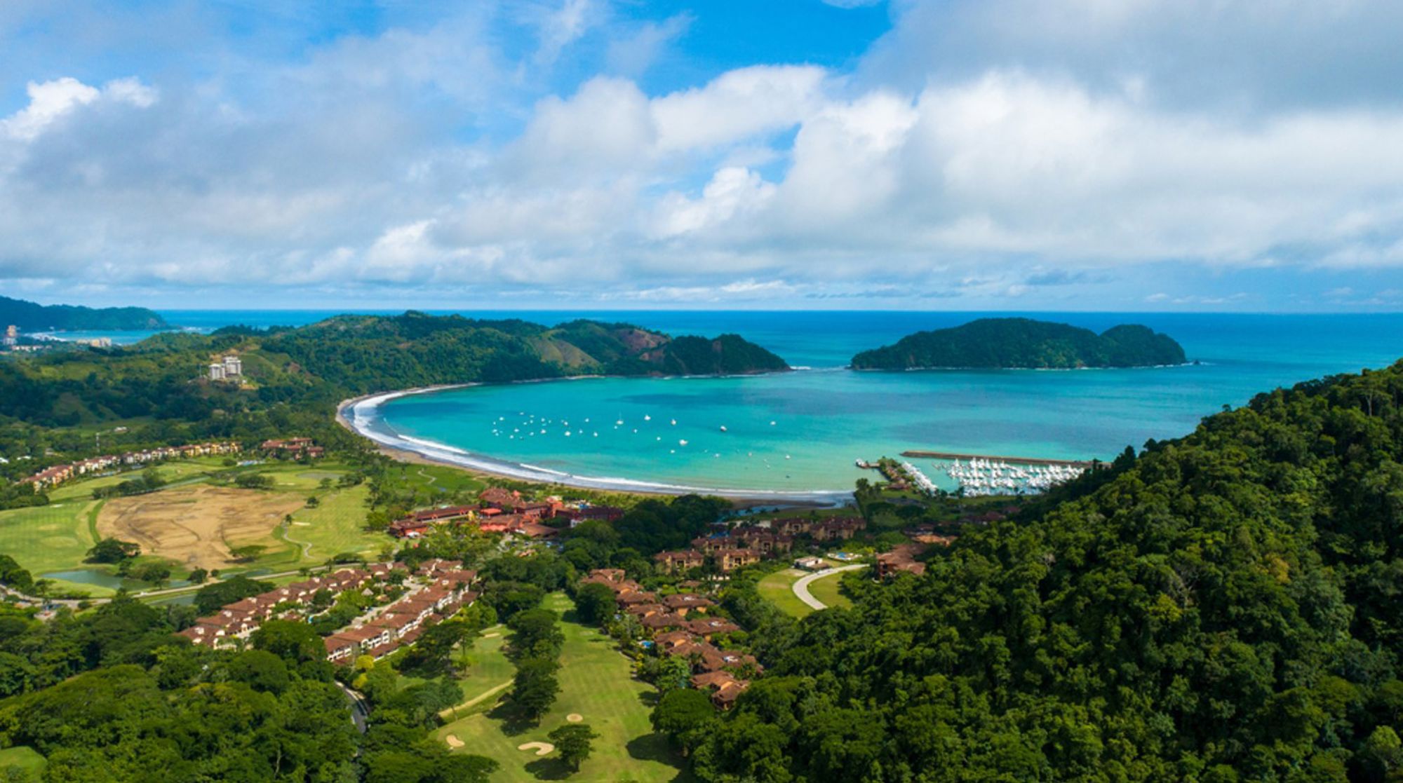 Panoramisch uitzicht op een baai met strand, jachthaven en groene heuvels aan de kust van Costa Rica.
