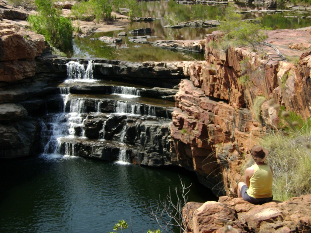 Reiziger kijkt uit over waterval en rotskloven in West-Australië tijdens groepsrondreis.