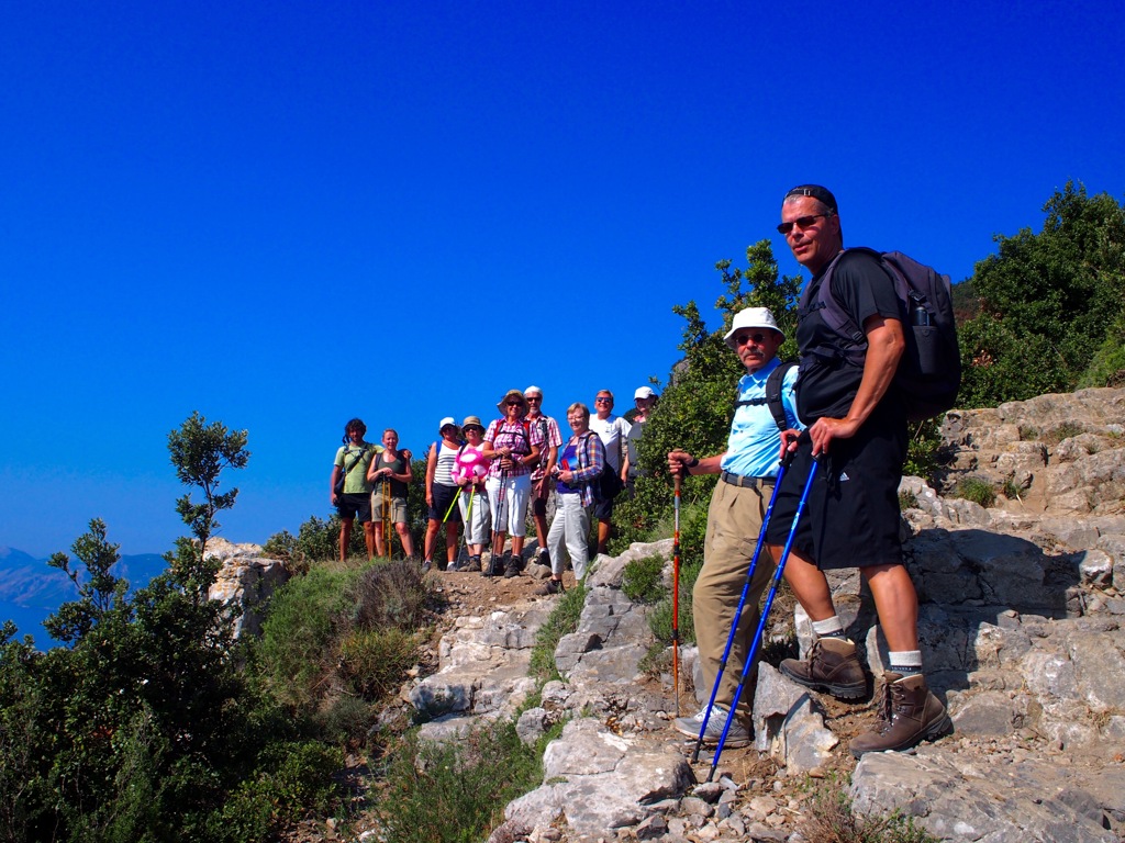 Groep wandelaars op rotsachtig bergpad aan de Amalfikust in Italië, met wandelstokken en rugzakken.
