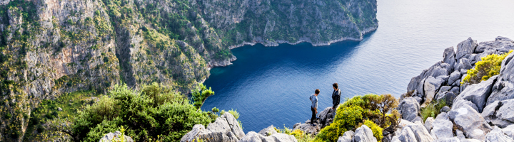 Wandelaars op rotsige kliffen met uitzicht op een blauwe baai in Turkije.