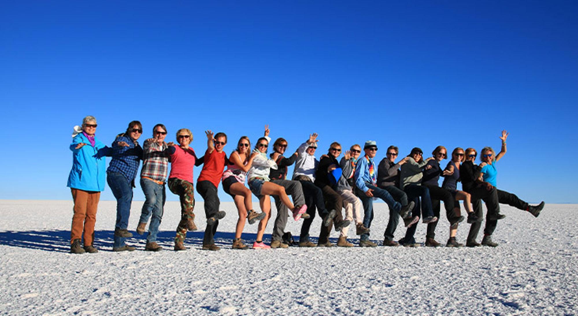 Uyuni Bolivia Groep reizigers poseert op een witte zoutvlakte onder een heldere blauwe lucht.