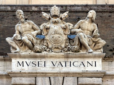 Beeldhouwwerk boven de ingang van de Vaticaanse Musea in Rome, met de tekst “MVSEI VATICANI”.