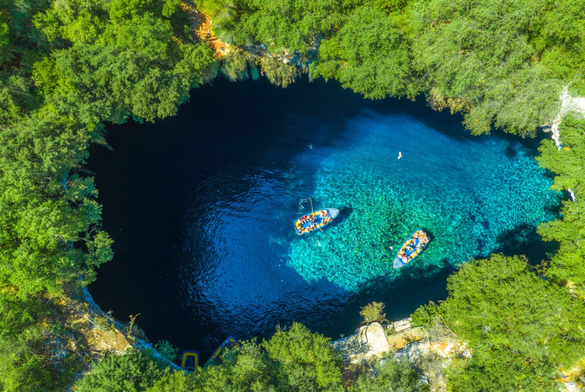 Melissani-grotmeer op Kefalonia, Griekenland, met bootjes op helderblauw water omringd door groen.