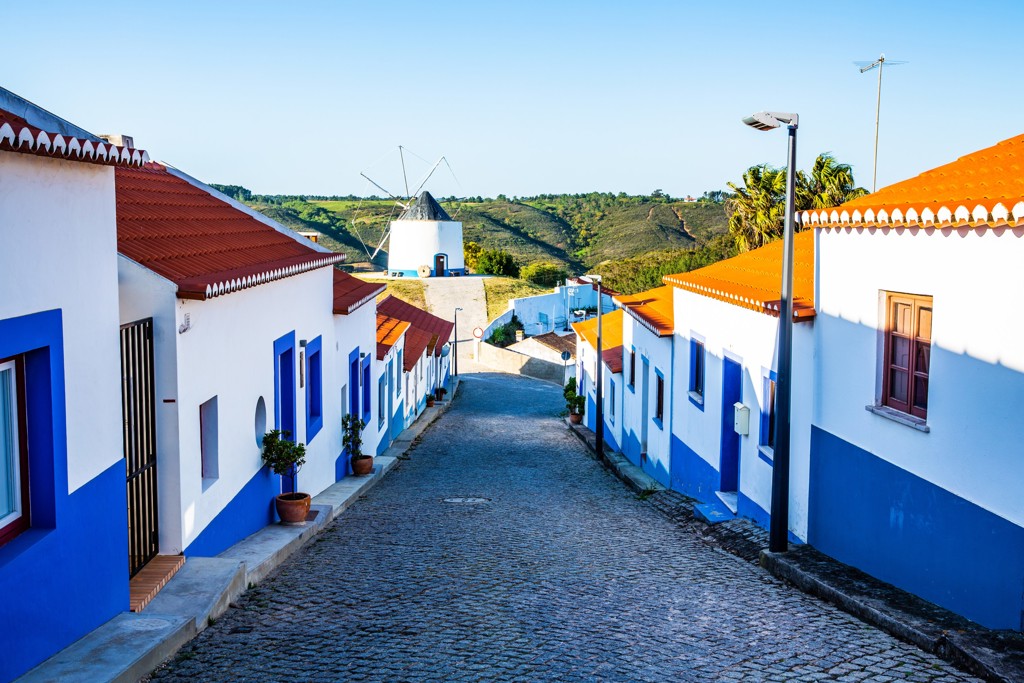 Straat met wit-blauwe huizen en windmolen in de Alentejo, Portugal, tijdens een wandelvakantie langs de Costa Vicentina.