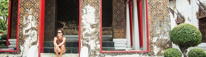 Bezoeker bij de ingang van een tempel in Bangkok met rood omlijste deuren en sierlijke muurschilderingen.