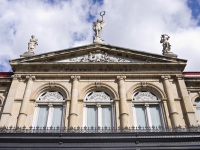 Gevel van Teatro Nacional in San José, Costa Rica, met beelden op het dak tegen een blauwe lucht.