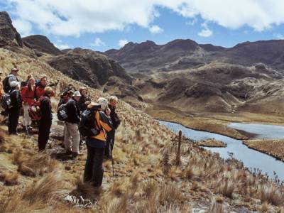 Wandelaars met rugzakken in het Andesgebergte van Ecuador, met uitzicht op een bergmeer en ruig landschap.