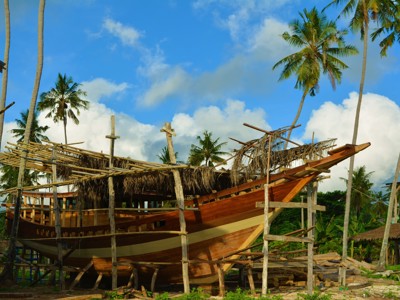Traditionele houten boot in aanbouw op Sulawesi, omringd door palmbomen.