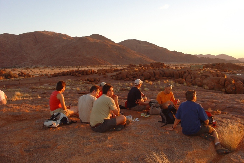 Groepsreis Zuidelijk Afrika: reizigers genieten van zonsondergang in rotsachtig woestijnlandschap in Namibië.