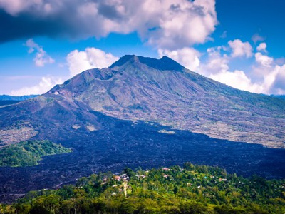 Uitzicht op de vulkaan Mount Batur op Bali, met lavavelden en groene heuvels onder een blauwe lucht.