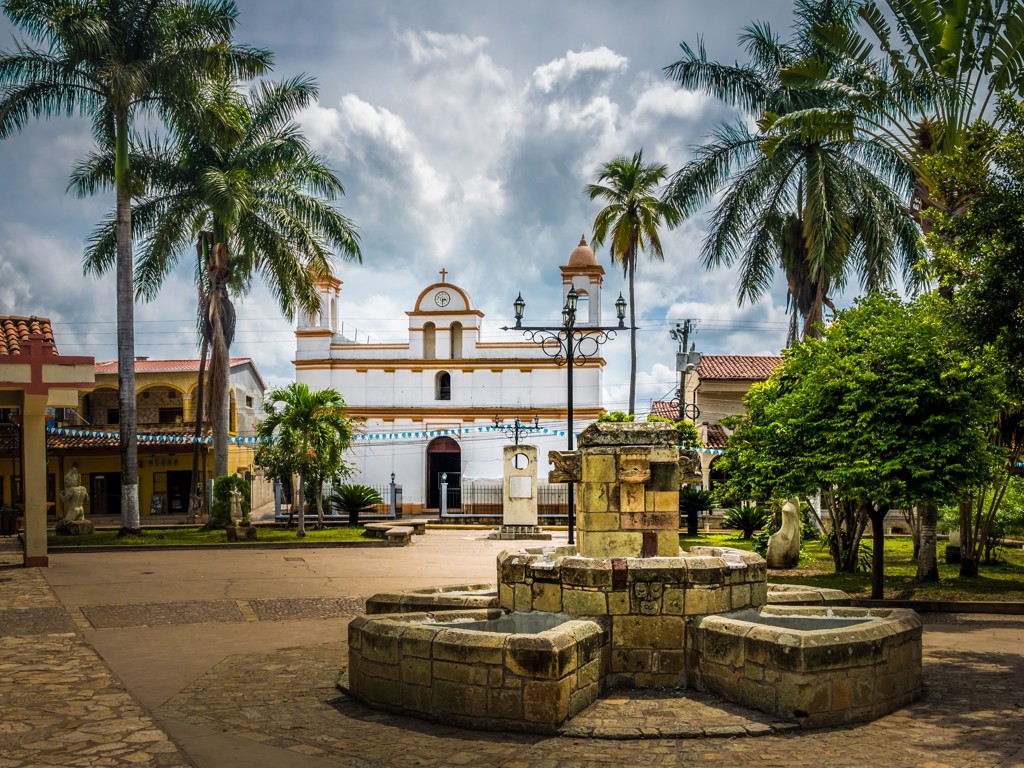 Plein met fontein en witte kerk tussen palmbomen tijdens 22-35ers reis Guatemala, Honduras en El Salvador.