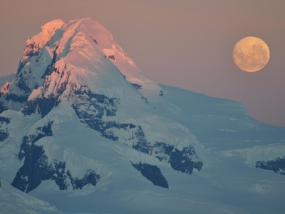 Besneeuwde bergtop in Antarctica bij zonsondergang met volle maan.