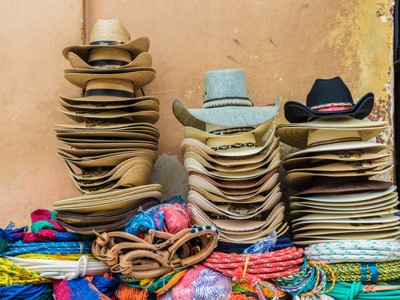 Stapel sombrero’s en cowboyhoeden op een markt, met kleurrijke touwen en lederen riemen in Guatemala.