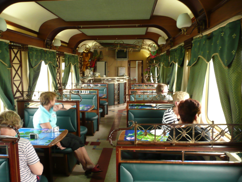 Interieur van de restauratiewagon van de Trans-Siberië Expres met zitbanken, tafels en reizigers.