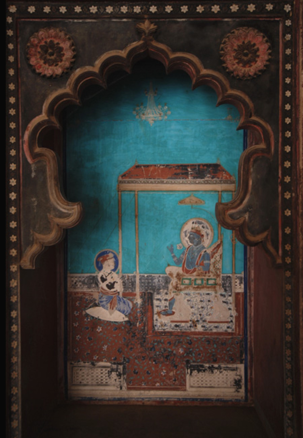 Muurschildering in Noord-India met traditionele figuren in een nis met boogvormig ornament.