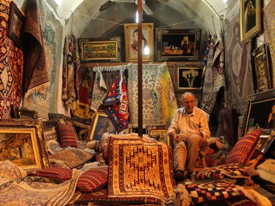 Tapijtenwinkel in Iran met kleurrijke Perzische tapijten en kussens, met verkoper tussen de tapijten.