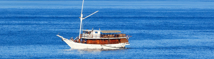 Houten zeilboot vaart over een kalme, blauwe zee.