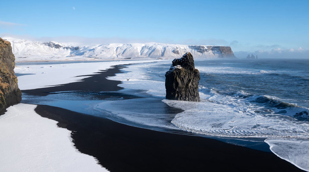 Zwart zandstrand met sneeuw en basaltrotsen aan de kust van IJsland in de winter.