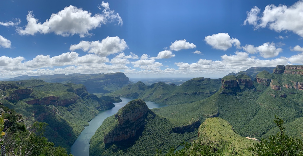 Panorama over de Blyde River Canyon in Zuid-Afrika met kronkelende rivier en groene bergen onder blauwe lucht.