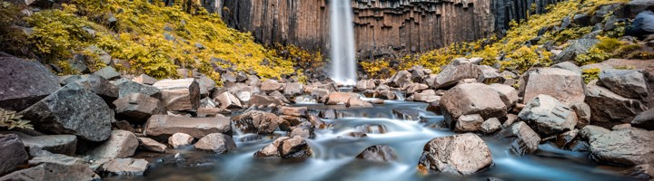 Svartifoss-waterval bij Skaftafell, omringd door basaltkolommen en een rotsige rivierbedding.