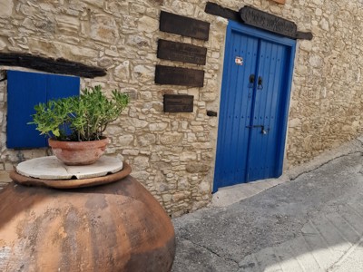 Stenen gevel met blauwe deur en grote aardewerken kruik in een Cypriotisch dorp op Route Cyprus.